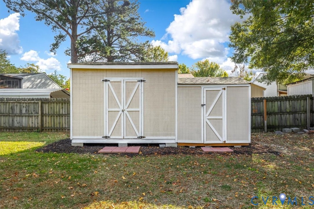 External storage structure featuring dual entry doors, shingle roofing, and concrete block foundation pads set on a mulched perimeter
