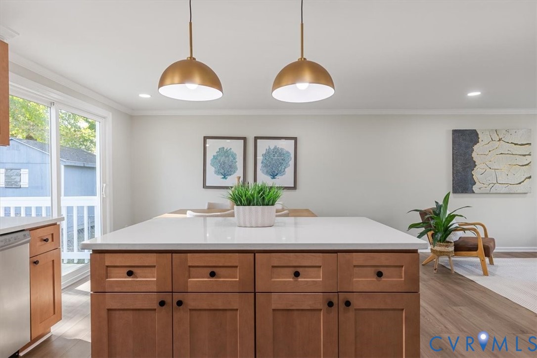 Kitchen island with light-toned countertop and wood-finish cabinetry, paired with dual metallic pendant lighting, wood-finish flooring, and sliding glass door
