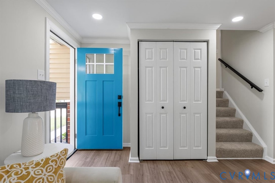 Entryway featuring a vibrant blue front door with a glass pane, wood-finish flooring, recessed lighting, double-door closet with six-panel doors, and staircase with a matte black wall-mounted handrail Entryway featuring a vibrant blue front door with a glass pane, wood-finish flooring, recessed lighting, double-door closet with six-panel doors, and staircase with a matte black wall-mounted handrail