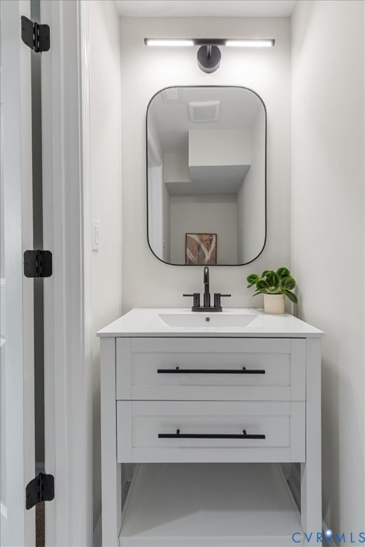 White vanity featuring two storage drawers, matte black hardware, a rectangular sink, and a white countertop, complemented by a black-framed rounded mirror, a linear wall-mounted light fixture, and a widespread matte black faucet