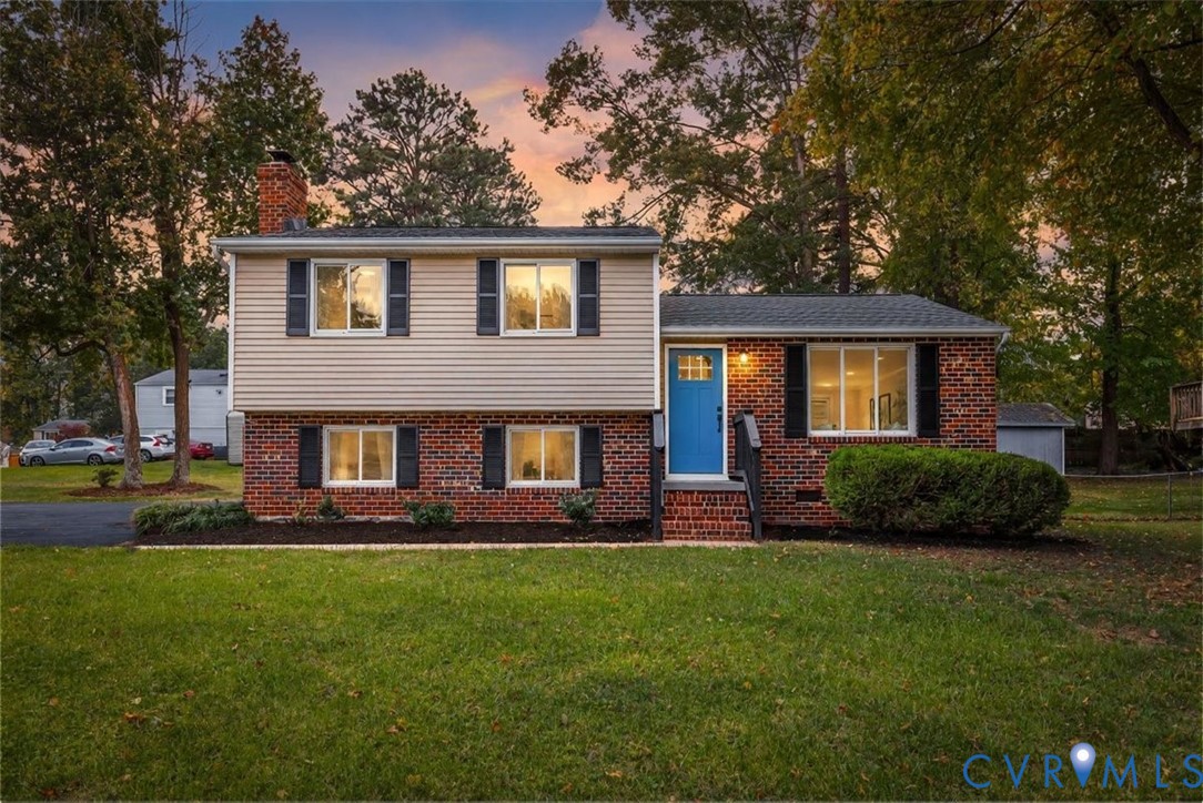 Split-level exterior featuring a brick and horizontal siding facade, multiple windows with dark shutters, a front entry door with a glass inlay, and a covered brick stoop