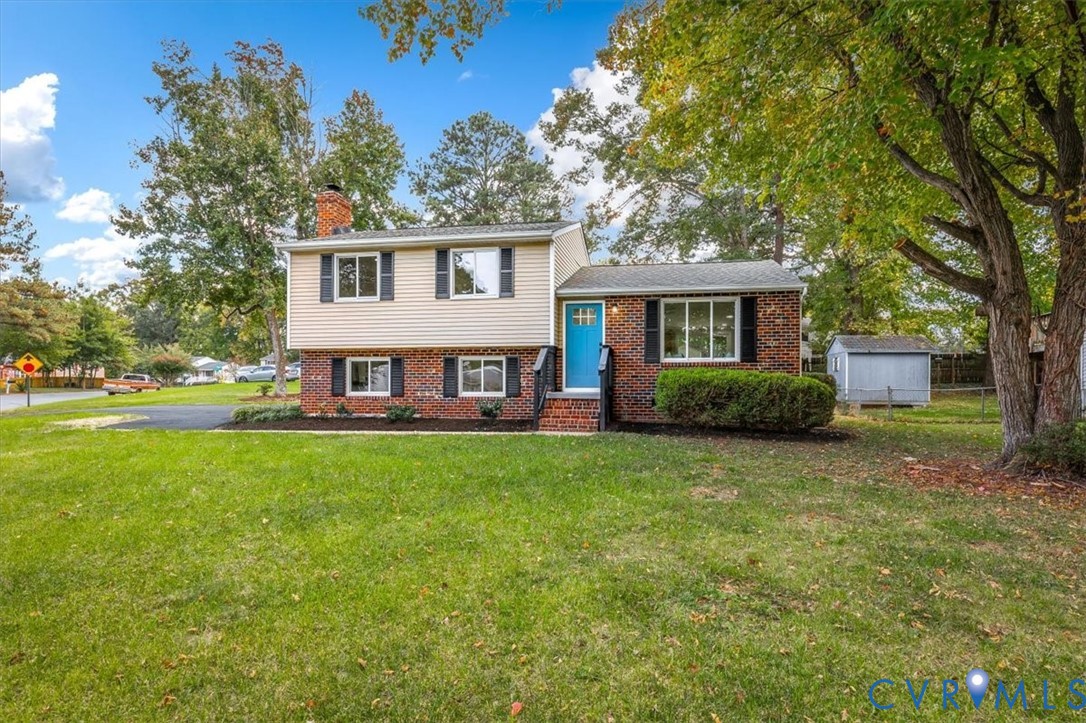 Split-level exterior featuring a brick and vinyl siding faade, chimney, asphalt driveway, and detached storage structure on a manicured lawn