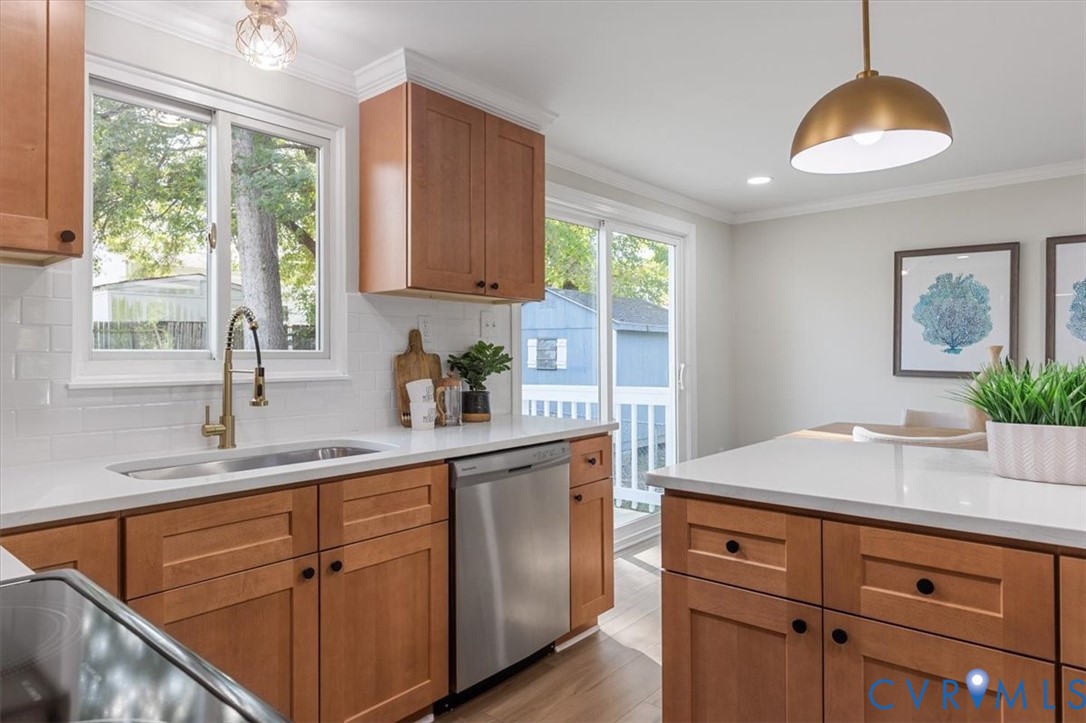 Kitchen featuring shaker-style cabinetry, quartz countertops, white subway tile backsplash, stainless steel dishwasher, and brass-tone pendant lighting