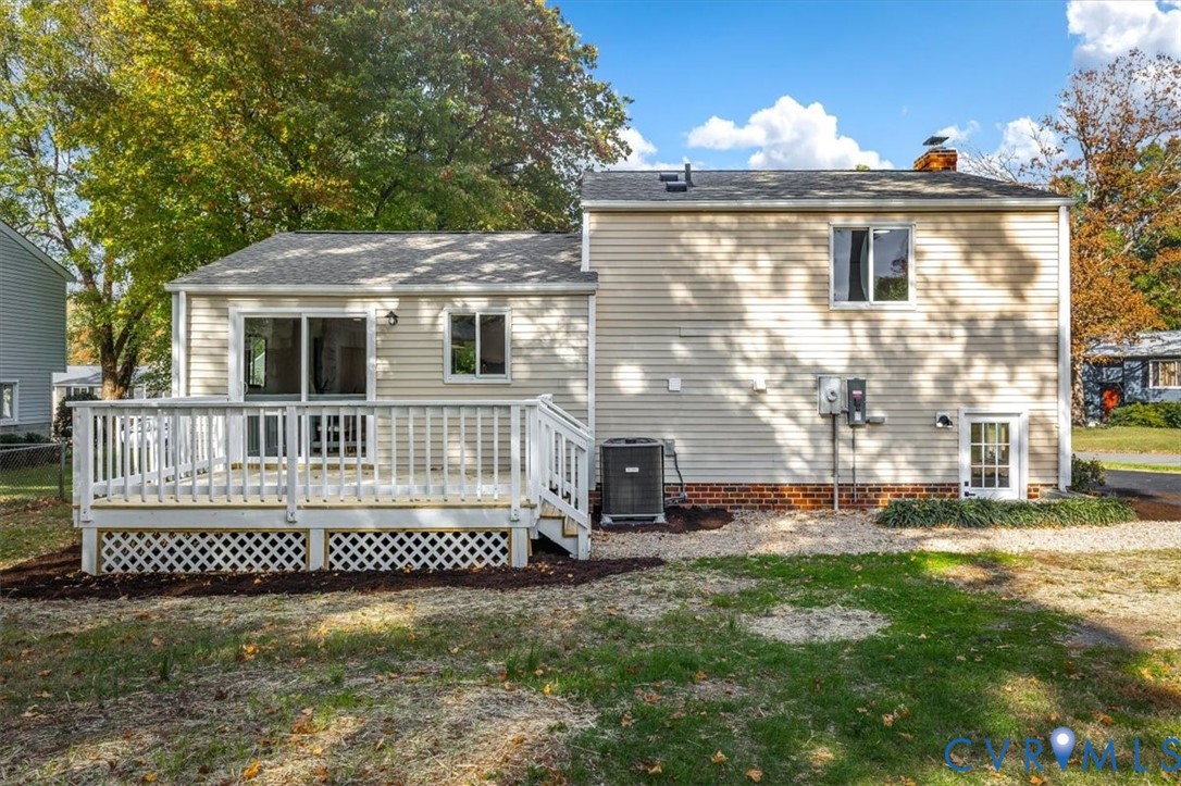 Rear exterior featuring light-toned horizontal siding, a white wooden deck with lattice skirting, sliding glass doors, and a brick foundation trim