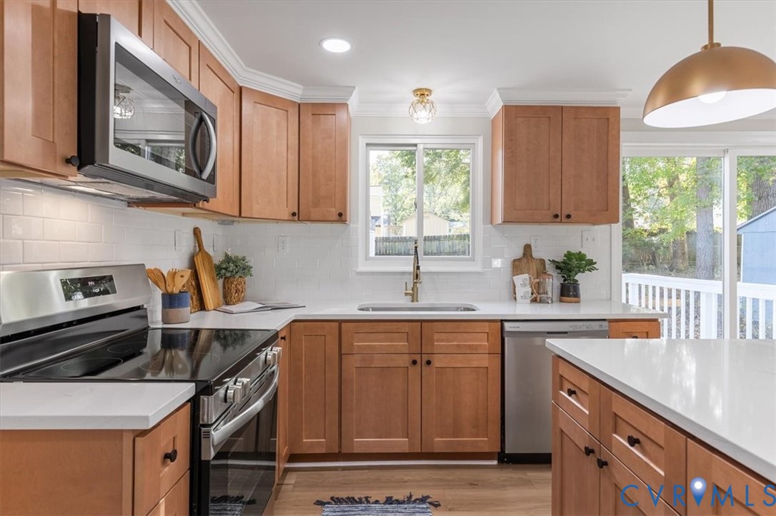 Kitchen featuring warm-tone wood cabinetry, white stone countertops, a white subway tile backsplash, stainless steel appliances, and a polished metal pendant light