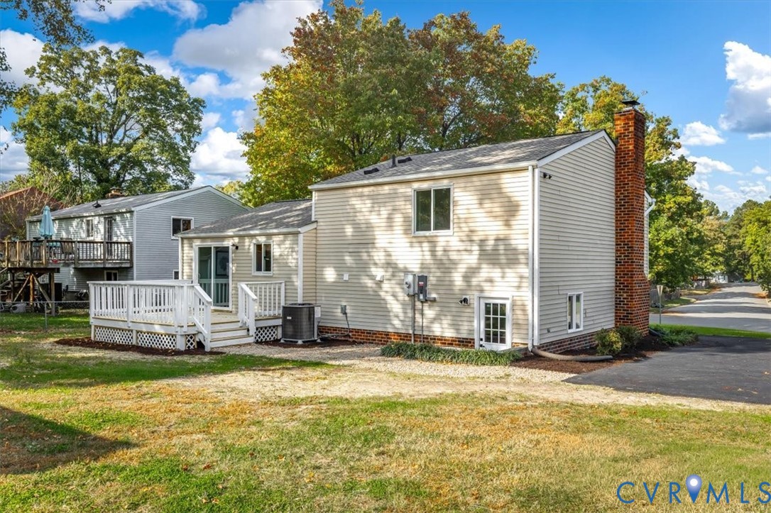 Exterior featuring light-toned horizontal siding, a raised wood deck with white lattice skirting, a classic red brick chimney, and an asphalt driveway