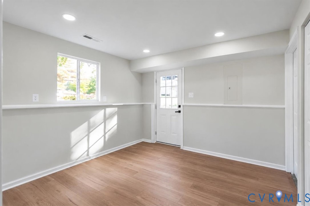 Interior space featuring wood-finish flooring, recessed lighting, neutral wall paint, a single-hung window with a chair rail, and an exterior door with a multi-pane glass insert