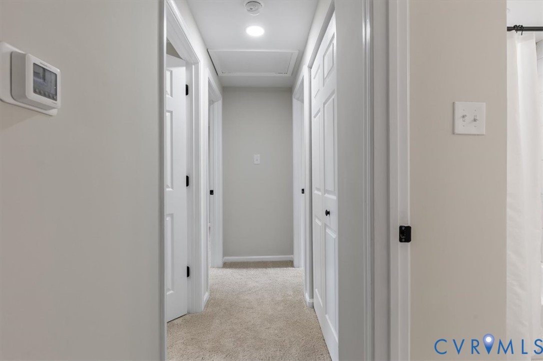 Hallway featuring neutral wall paint, carpeted flooring, multi-panel interior doors, and a ceiling-mounted attic access panel