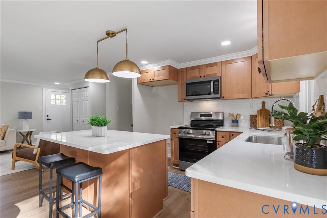 Kitchen featuring wood cabinetry, white stone-finish countertops, subway tile backsplash, a central island, and matte metallic pendant lighting