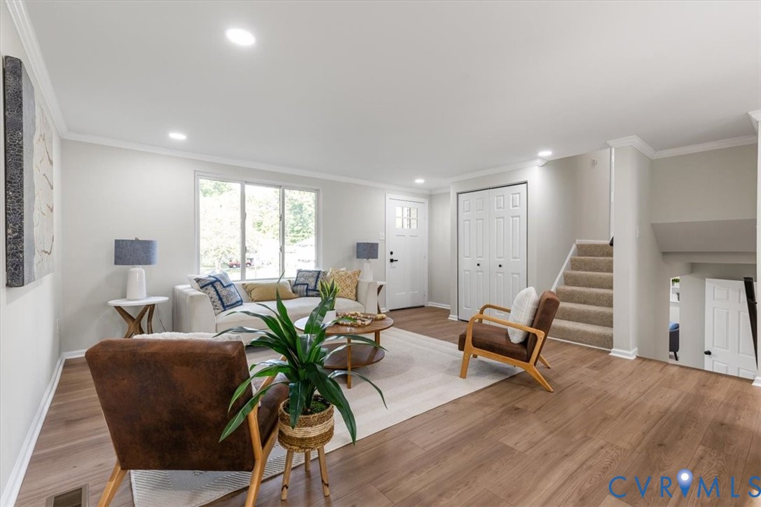 Neutral-toned interior featuring wood-finish flooring, recessed lighting, crown molding, double-door closet, and carpeted staircase Neutral-toned interior featuring wood-finish flooring, recessed lighting, crown molding, double-door closet, and carpeted staircase