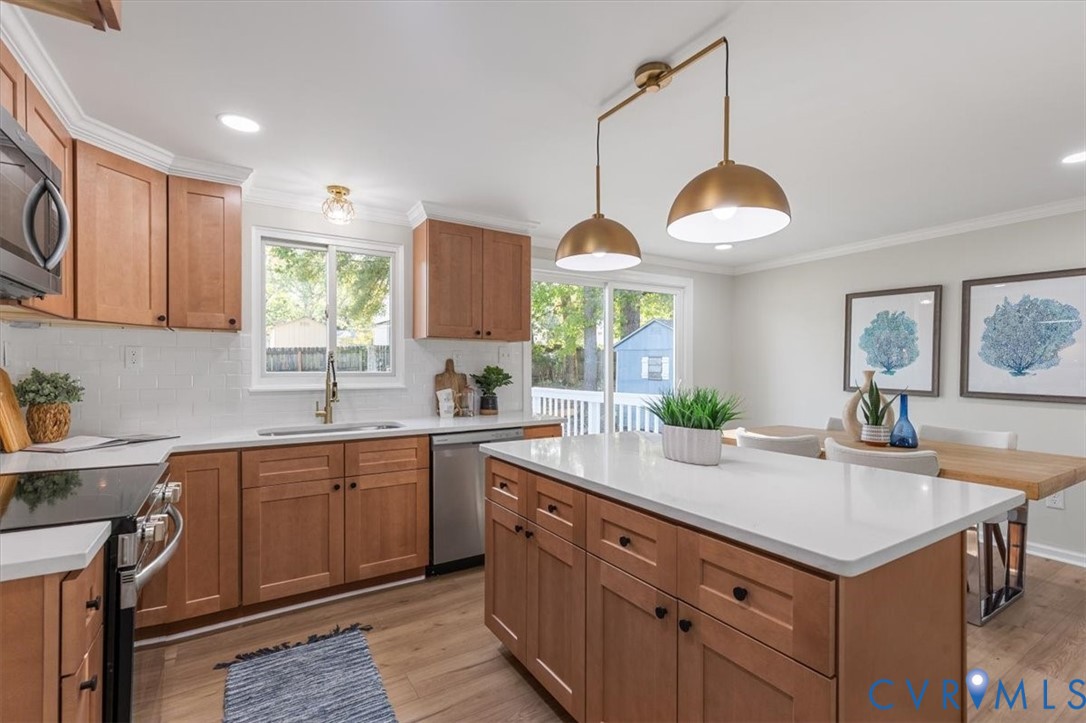 Kitchen featuring wood cabinetry, a central island with a solid-surface countertop, wood-finish flooring, and dual pendant lighting