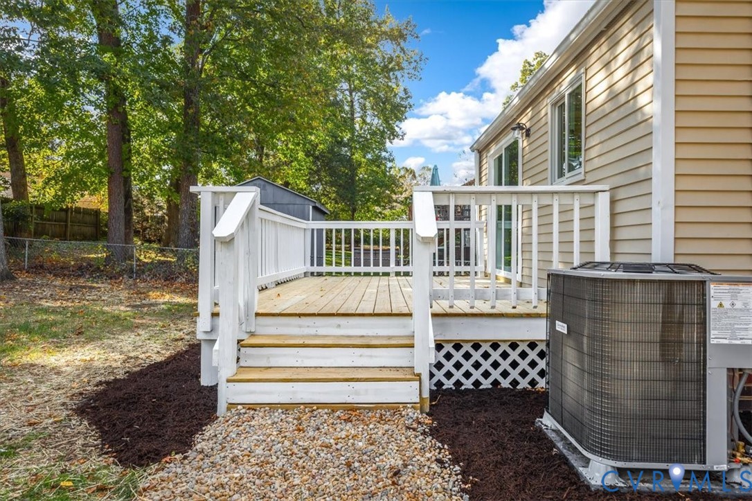 Exterior wood deck featuring white railing and lattice skirting, gravel walkway, vinyl siding, and mature trees