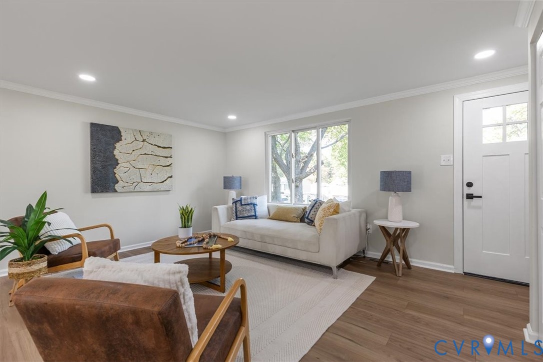 Neutral-toned living space featuring wood-finish flooring, recessed lighting, crown molding, and a multi-lite exterior entry door Neutral-toned living space featuring wood-finish flooring, recessed lighting, crown molding, and a multi-lite exterior entry door