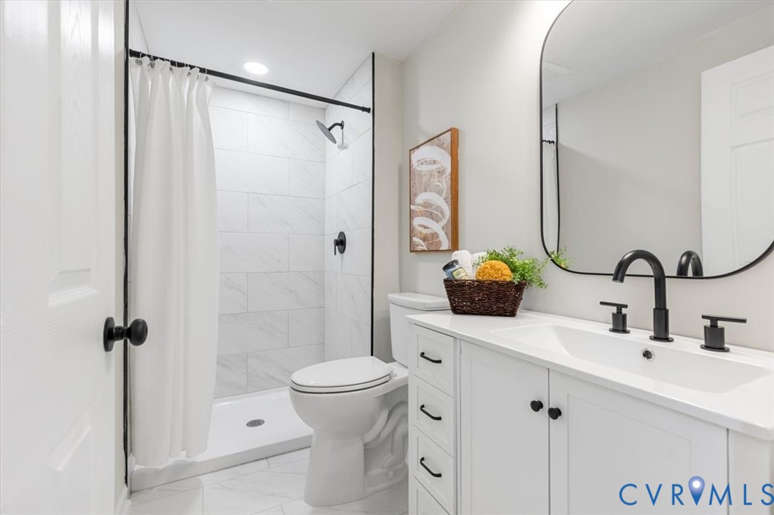 Bathroom featuring a white vanity with drawers, a rectangular undermount sink, a matte black widespread faucet, a wall-mounted arched mirror, and a walk-in shower with white tile surround and matte black fixtures