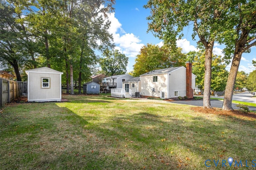 Expansive backyard featuring a detached storage shed, mature trees, wood privacy fencing, and a raised wooden deck