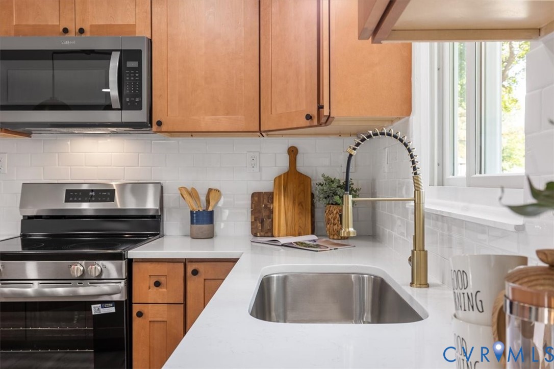 Kitchen featuring wood cabinetry, white quartz countertops, subway tile backsplash, stainless steel appliances, and a gold-finish arched faucet