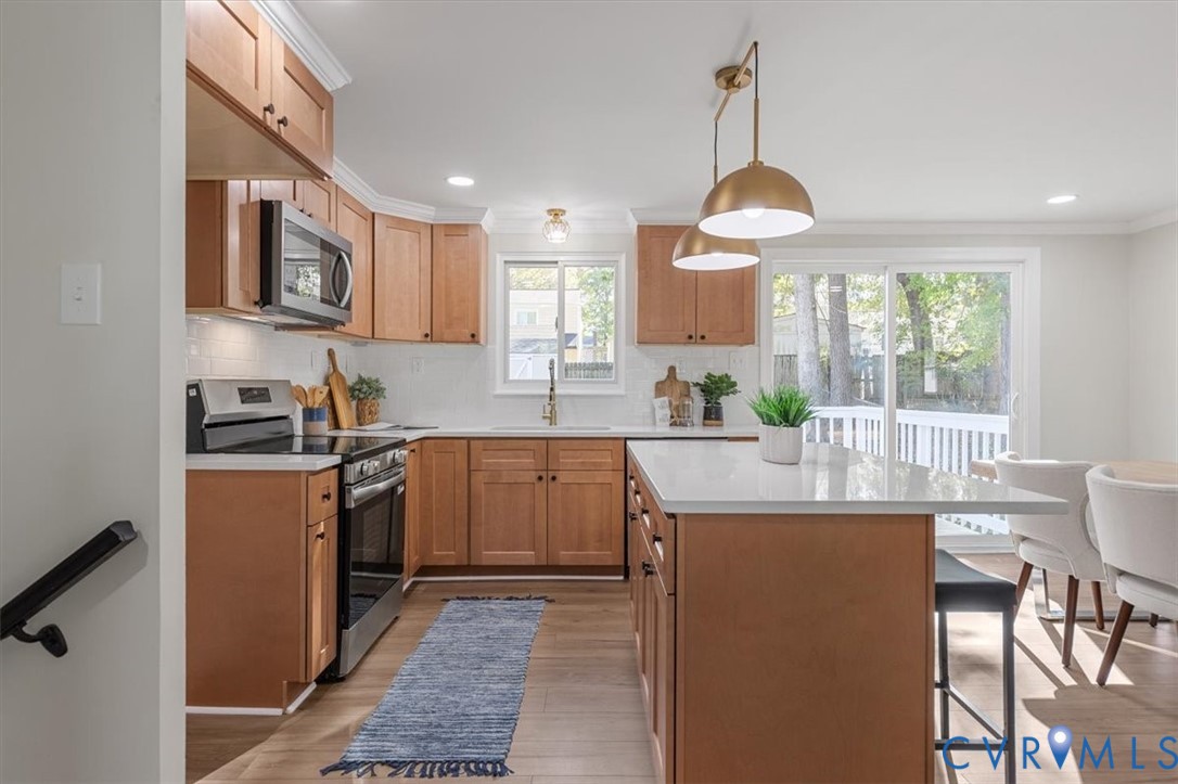 Kitchen featuring wood cabinetry, an island with a light-toned countertop, stainless steel appliances, recessed ceiling lighting, and pendant fixtures