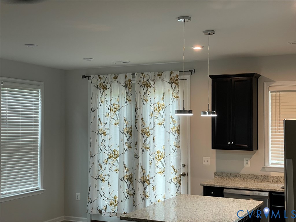 Kitchen featuring dark-finish cabinetry, stone-texture countertops, dual modern pendant lighting, and horizontal slatted window blinds