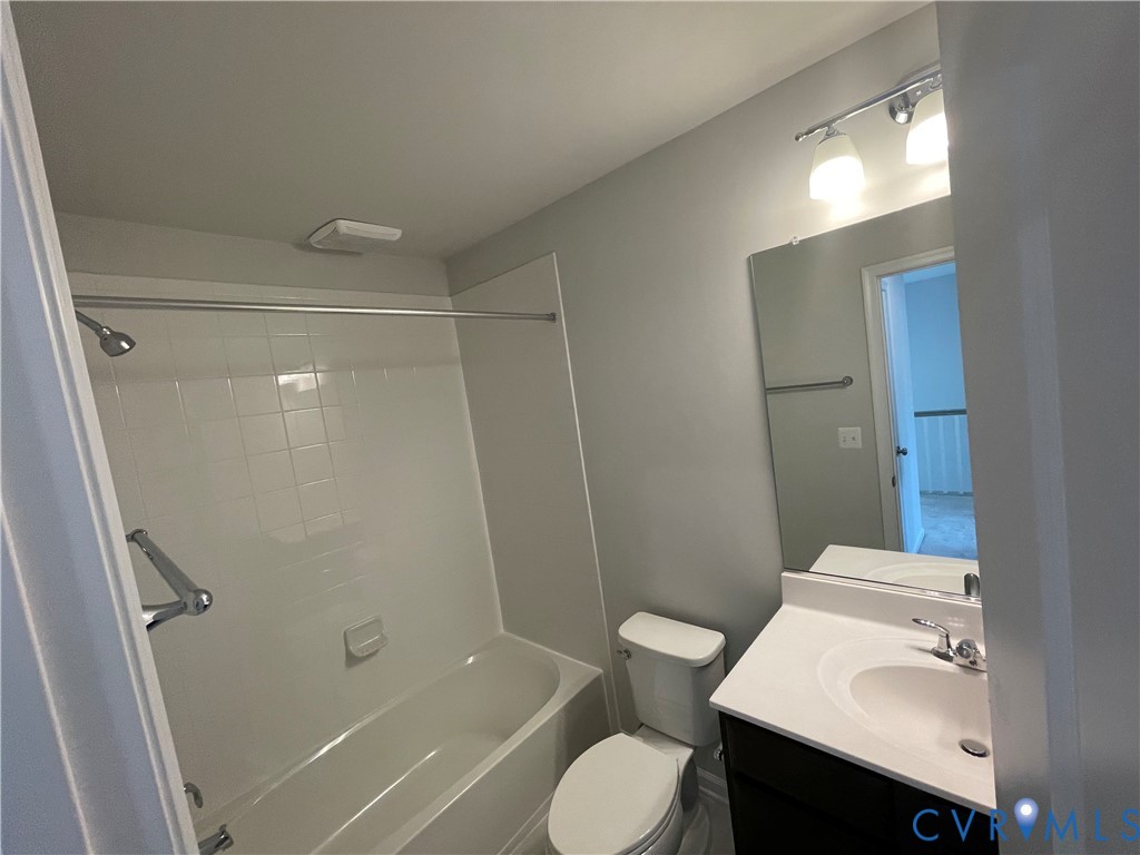 Bathroom featuring a tub-shower combination with white tile surround, vanity with an integrated countertop sink, wall-mounted mirror, and polished metal hardware