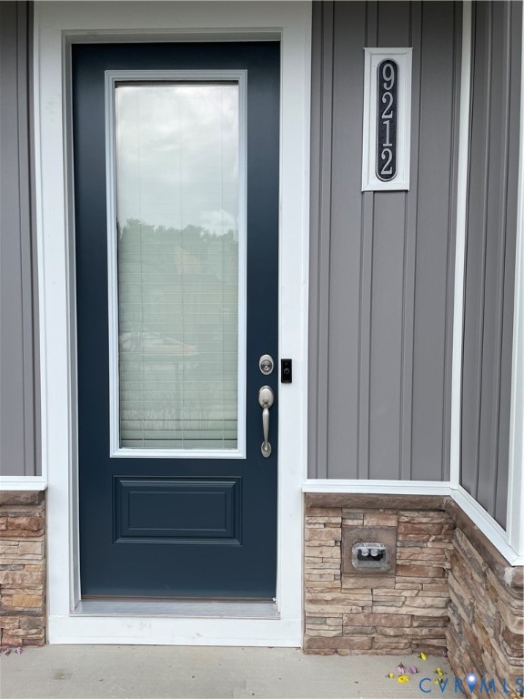 Entryway featuring a dark-finish door with an integrated glass panel, vertical panel siding, stone veneer wainscoting, and a vertical address plaque