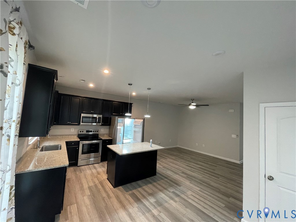 Kitchen featuring dark cabinetry, stone-finish countertops, stainless steel appliances, a center island with dual pendant lighting, and wood-finish flooring