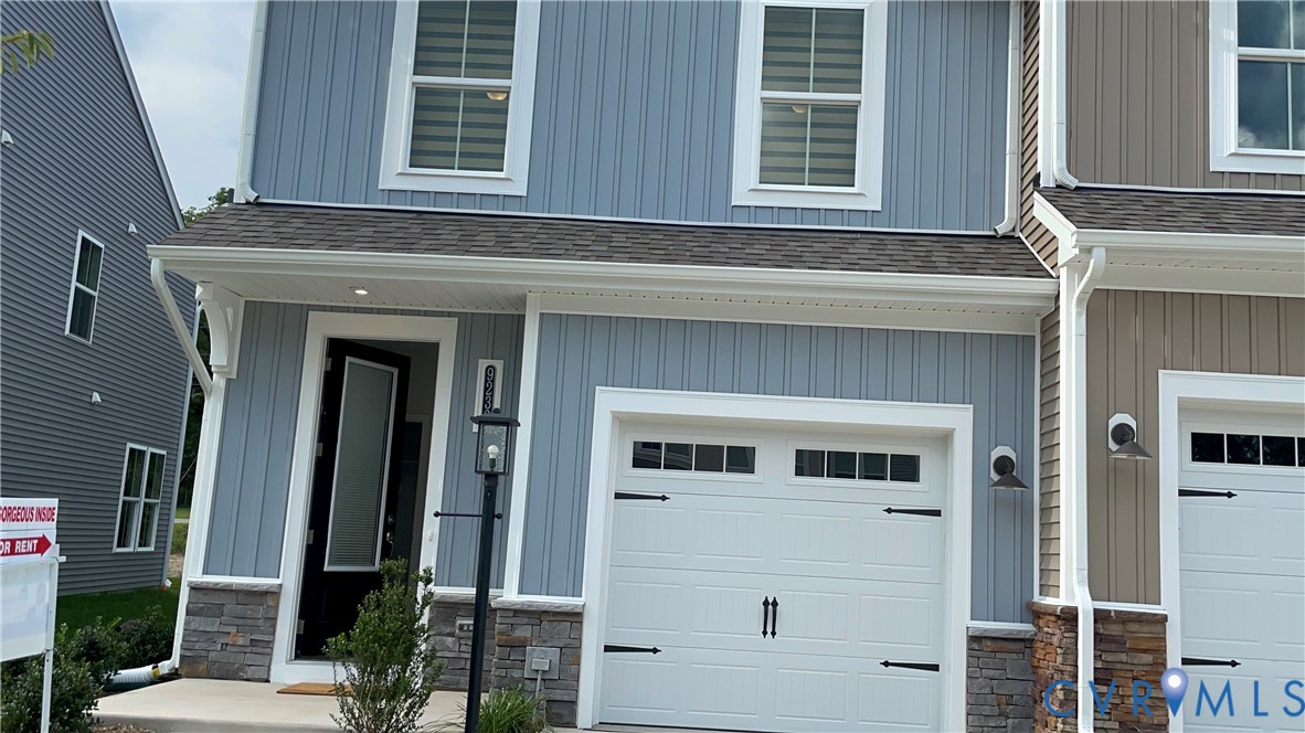 Vertical board-and-batten siding with stone veneer base, single-car garage featuring carriage-style hardware, and covered front entryway