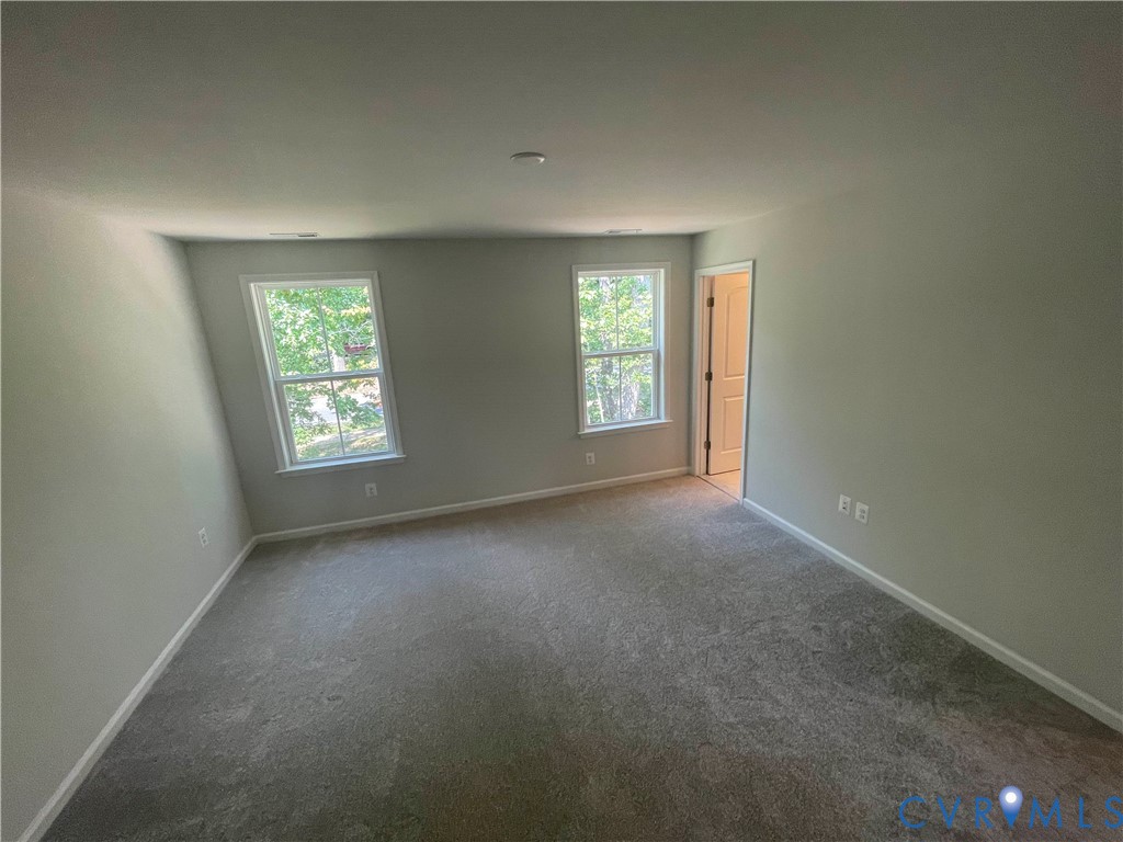 Room featuring neutral-toned carpeting, two double-hung windows, and a traditional six-panel interior door