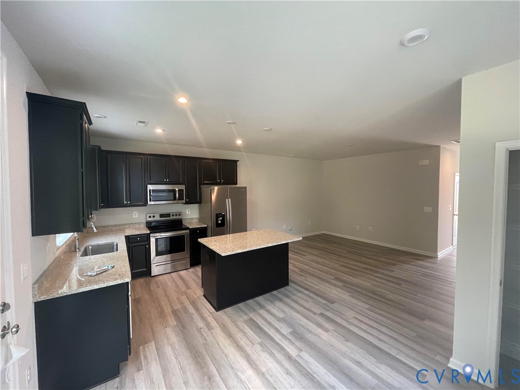 Kitchen featuring dark cabinetry, stone countertops, a center island, stainless steel appliances, and wood-finish flooring