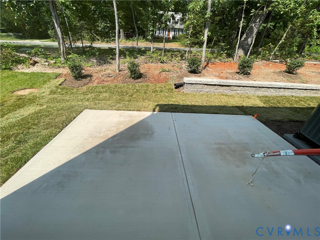 Concrete patio featuring a low-profile stone retaining wall and grass lawn
