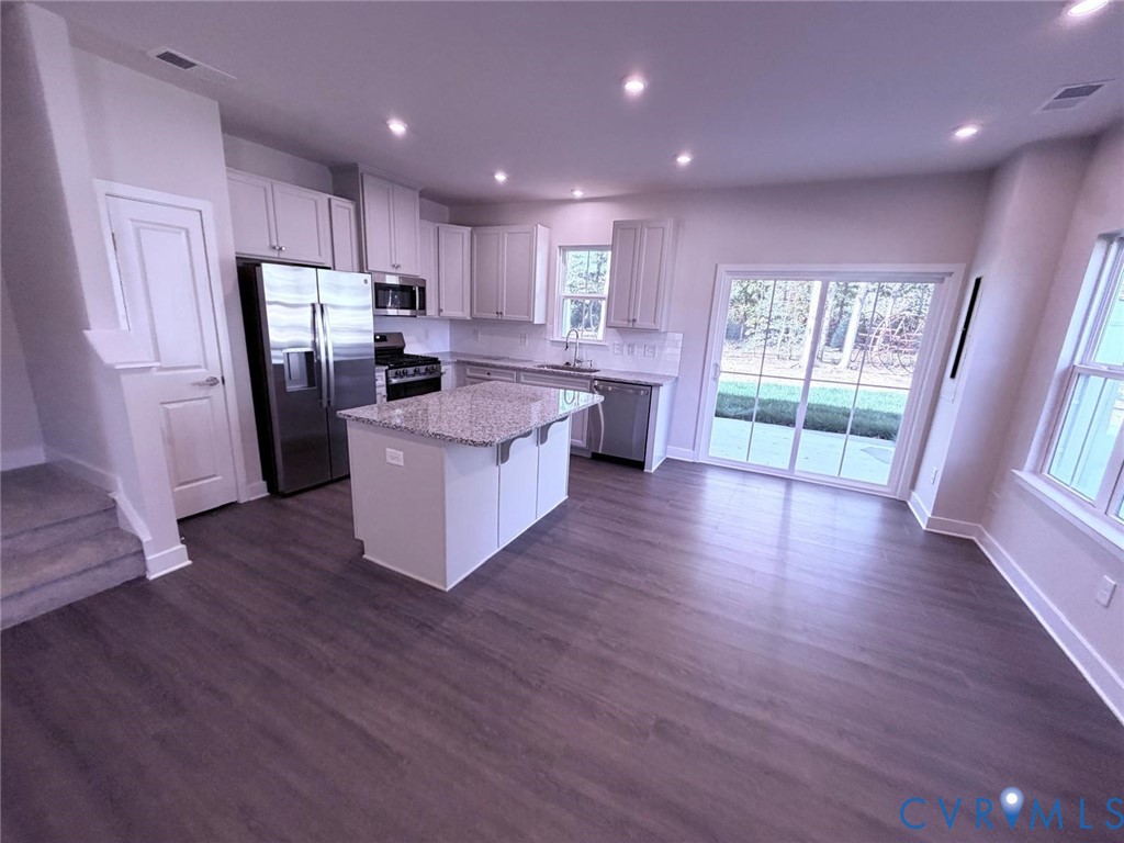 Kitchen featuring white cabinetry, stone-finish countertops, a central island, stainless steel appliances, and wood-finish flooring