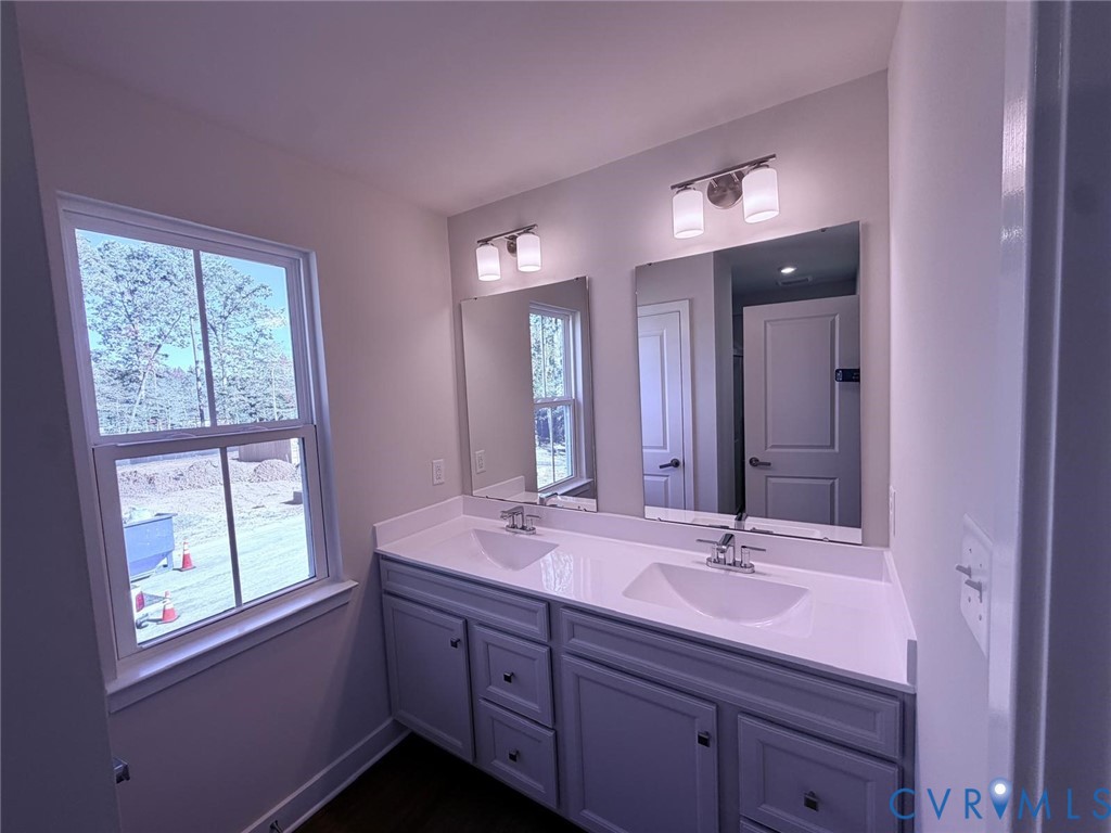 Double vanity featuring a stone countertop, dual integrated rectangular sinks, polished chrome fixtures, and shaker-style cabinetry with dual wall-mounted light fixtures