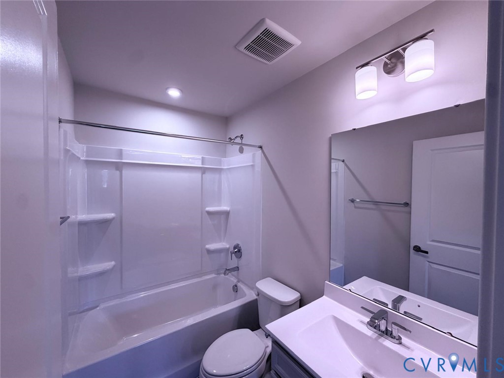 Bathroom featuring a tub and shower combination with integrated shelving, a rectangular vanity with a solid-surface countertop, a large wall-mounted mirror, and dual-light fixture
