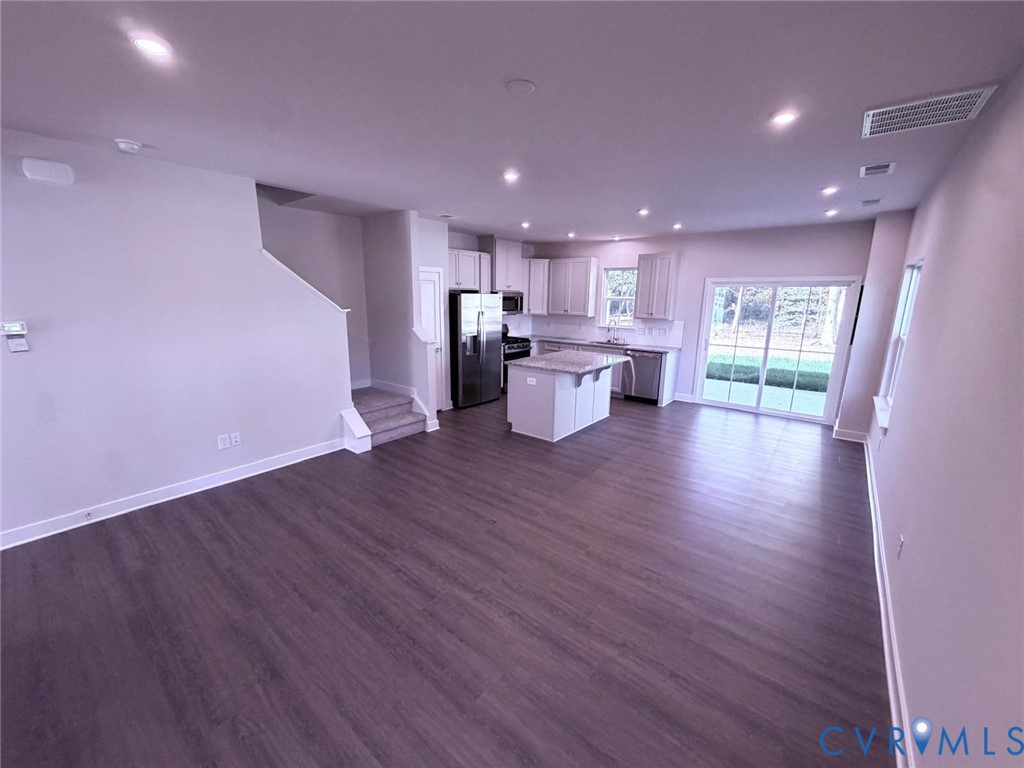 Open-concept interior featuring wood-finish flooring, recessed lighting, a kitchen island, stainless steel appliances, and a glass sliding door