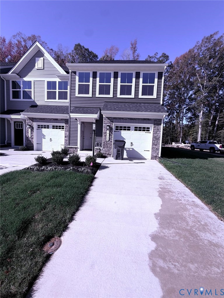 Townhome exterior featuring horizontal siding, stone veneer accents, a concrete driveway, and attached single-car garages