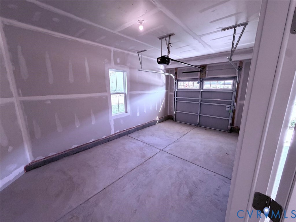 Interior garage space featuring concrete flooring, unpainted gypsum wallboard, a single-pane window, and an automated overhead door opener