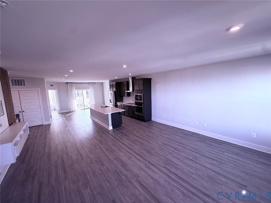 Open-concept kitchen featuring dark cabinetry, a central island with a light-toned countertop, built-in stainless steel appliances, and wood-finish flooring