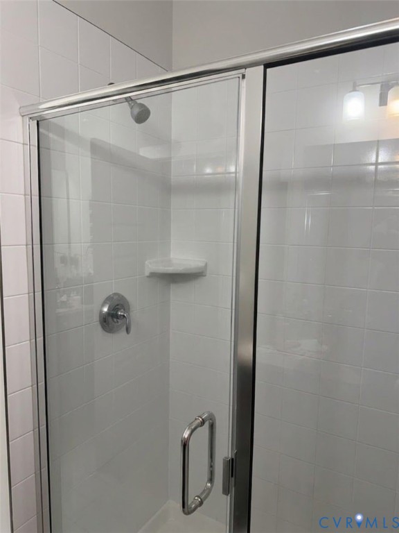Walk-in shower featuring white wall tile, a glass door with a polished metal frame, built-in corner shelving, and a single-handle faucet