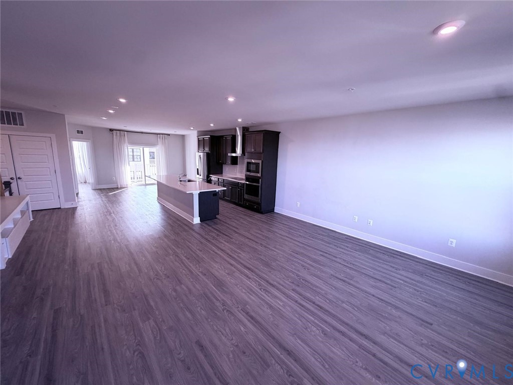 Open-concept interior featuring wood-finish flooring, recessed lighting, and a kitchen equipped with dark-toned cabinetry, an island with countertop seating, and a stainless steel range hood