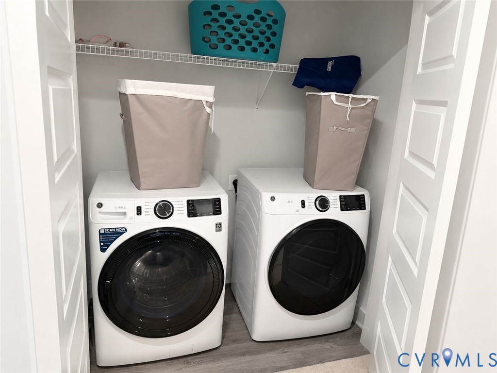 Laundry closet featuring dual white front-load appliances and overhead wire shelving, framed by white paneled doors
