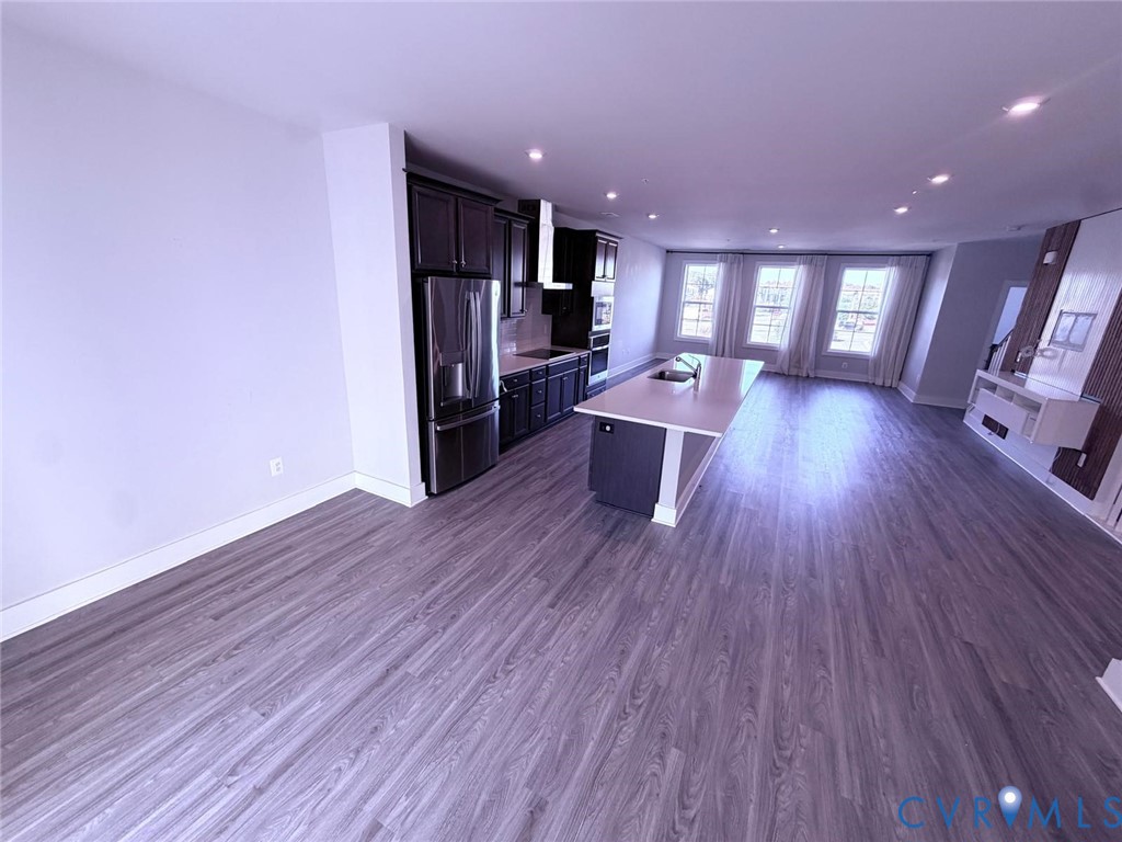 Kitchen featuring dark wood cabinetry, stainless steel appliances, a center island with a stone-finish countertop, and wood-finish flooring