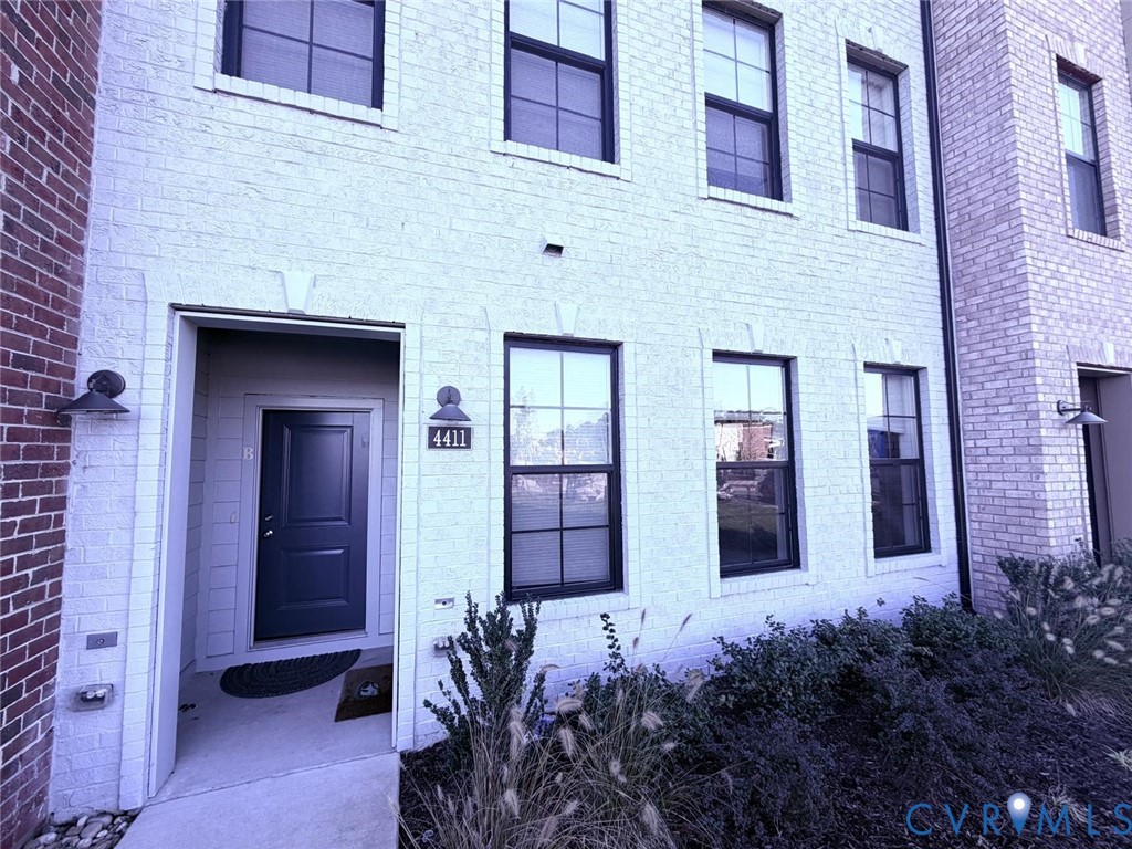 Exterior facade featuring painted brick masonry, grid-pane windows with dark frames, recessed entry, and wall-mounted exterior lighting