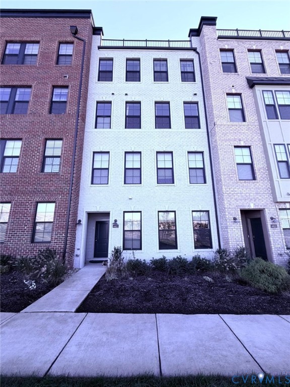 Four-story brick townhouse exterior featuring a rooftop terrace, dark-framed windows, and a dedicated concrete walkway Four-story brick townhouse exterior featuring a rooftop terrace, dark-framed windows, and a dedicated concrete walkway