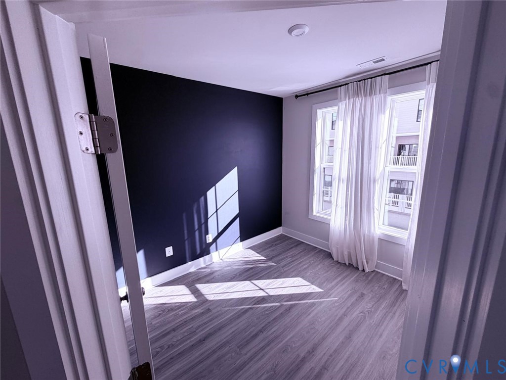 Room featuring wood-finish flooring, a charcoal accent wall, and dual windows with window casing