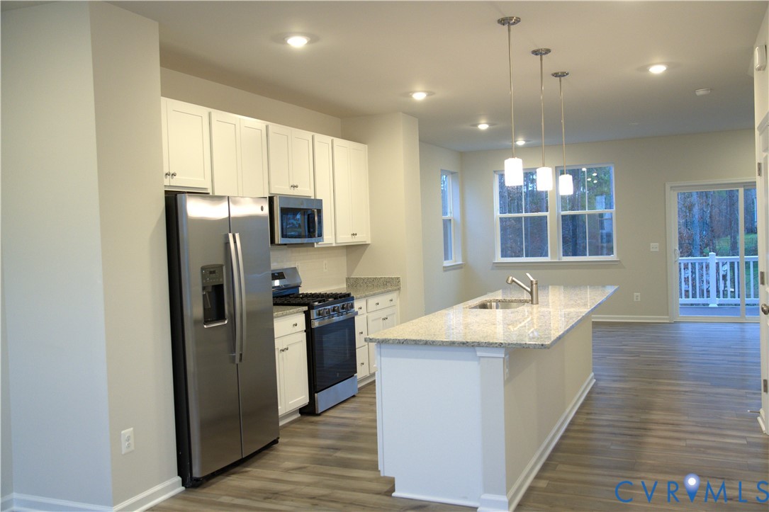 Kitchen featuring white cabinetry, stone-finish countertops, stainless steel appliances, a center island with a built-in sink, and wood-finish flooring Kitchen featuring white cabinetry, stone-finish countertops, stainless steel appliances, a center island with a built-in sink, and wood-finish flooring