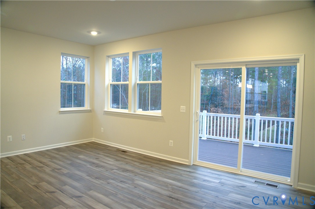 Neutral-toned interior featuring wood-finish flooring, multi-pane windows, recessed lighting, and a sliding glass door providing access to a deck with a white balustrade