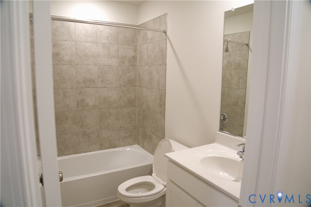 Bathroom featuring a white vanity with a composite countertop and integrated sink, a full-height wall-mounted mirror, and a tub with a surround of neutral-toned square tile