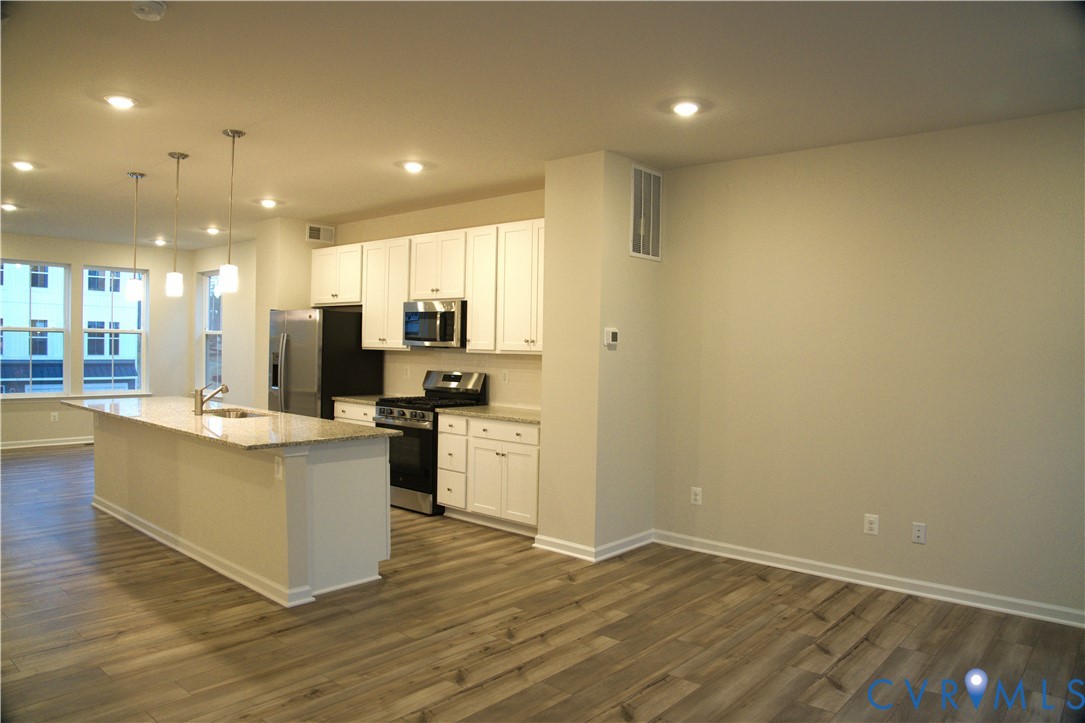 Kitchen featuring white cabinetry, stone-finish countertops, stainless steel appliances, a center island with an integrated sink, and wood-finish flooring Kitchen featuring white cabinetry, stone-finish countertops, stainless steel appliances, a center island with an integrated sink, and wood-finish flooring