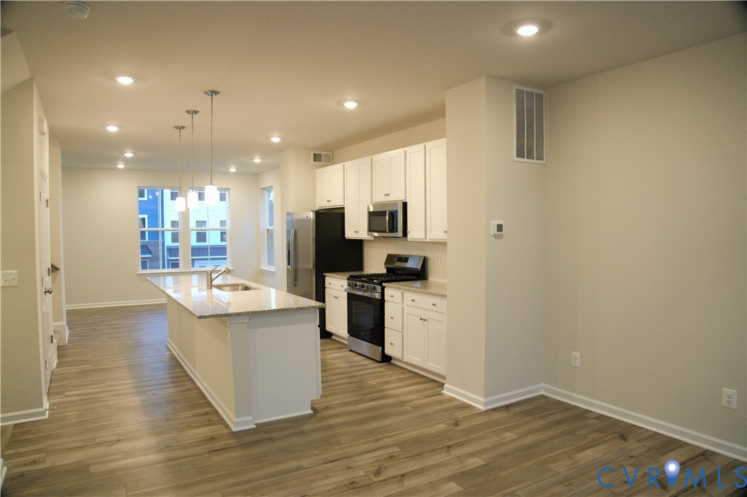 Kitchen featuring white cabinetry, stone-finish countertops, stainless steel appliances, a center island with pendant lighting, and wood-finish flooring Kitchen featuring white cabinetry, stone-finish countertops, stainless steel appliances, a center island with pendant lighting, and wood-finish flooring