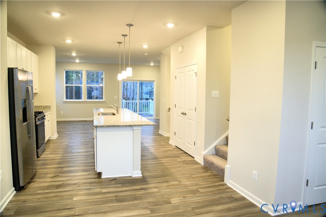 Kitchen featuring wood-finish flooring, a central island with stone-surface countertops, recessed lighting, pendant light fixtures, and stainless steel appliances Kitchen featuring wood-finish flooring, a central island with stone-surface countertops, recessed lighting, pendant light fixtures, and stainless steel appliances