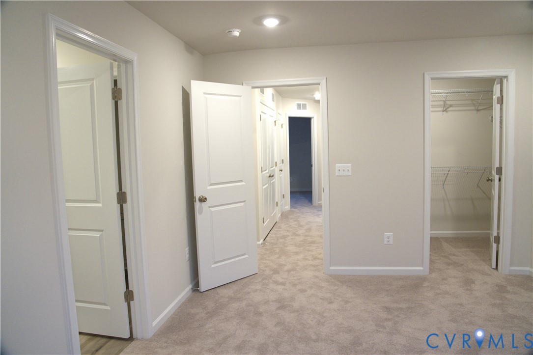 Interior space featuring neutral-toned carpeting, two-panel interior doors, and a walk-in closet with built-in wire shelving Interior space featuring neutral-toned carpeting, two-panel interior doors, and a walk-in closet with built-in wire shelving